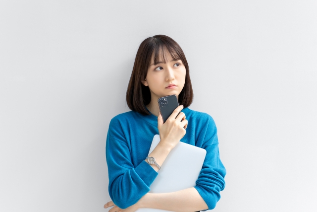 スマホとパソコンを持って悩む女性